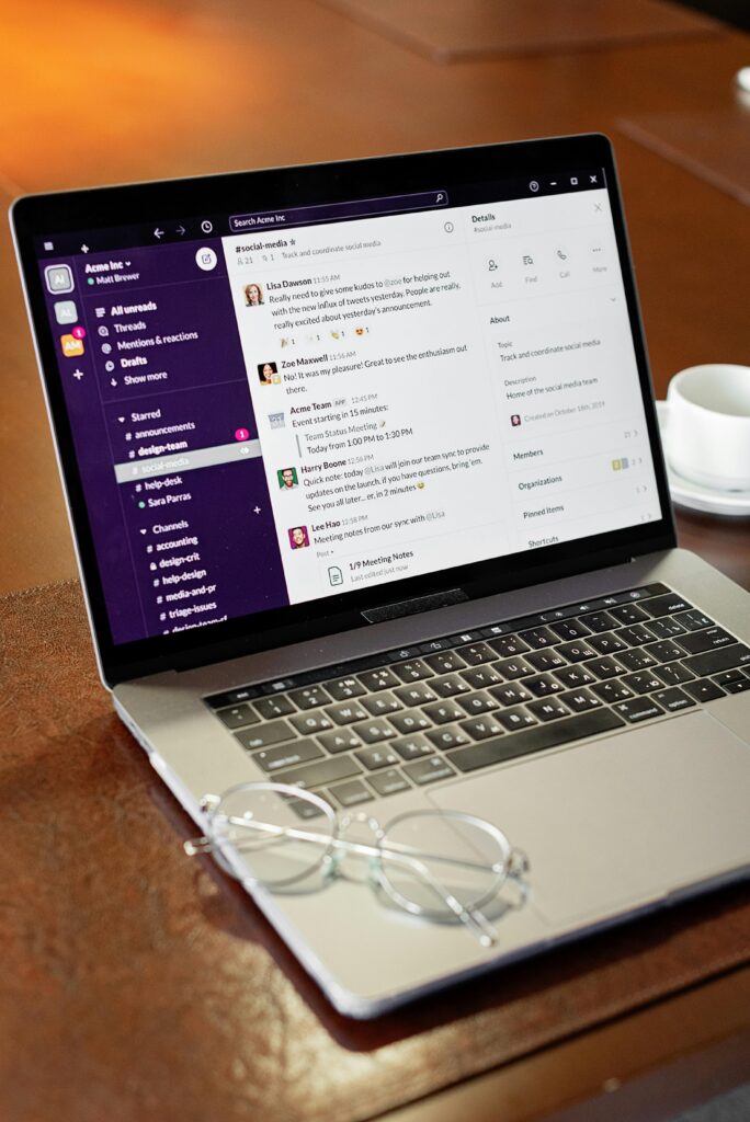 A laptop displaying a communication app next to eyeglasses and a coffee cup on a table.